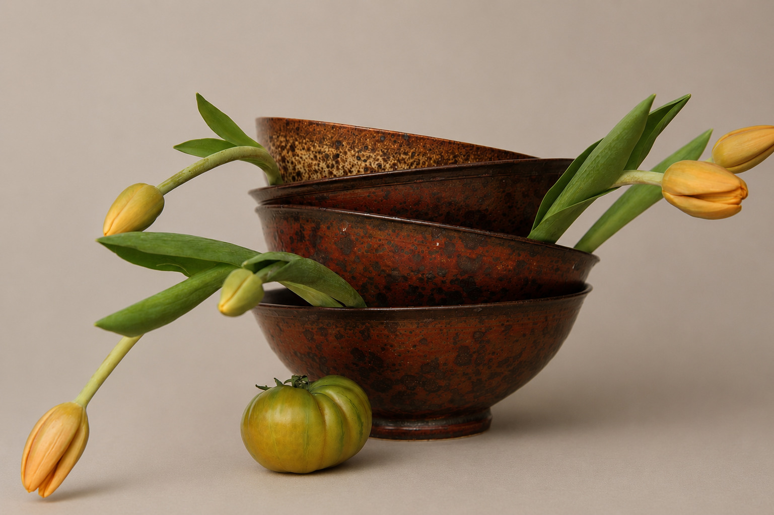 Stacked ceramic bowls with tulip stems and a green tomato